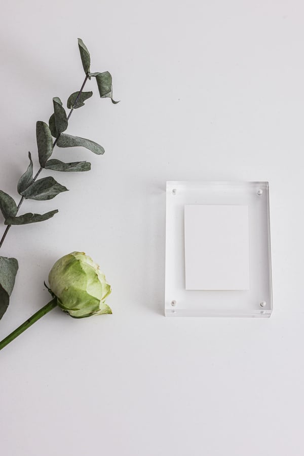 Tấm thẻ trắng kẹp giữa hai lớp mica trong đặt cạnh hoa hồng